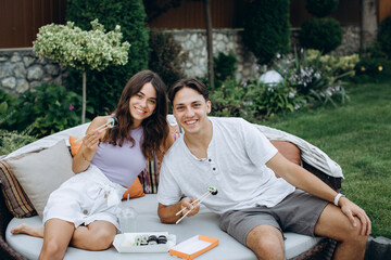 Young couple eating sushi sitting outdoors.