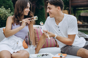 Young couple eating sushi sitting outdoors.