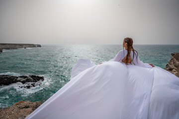 Happy freedom woman on the beach enjoying and posing in white dress. Rear view of a girl in a fluttering white dress in the wind. Holidays, holidays at sea.