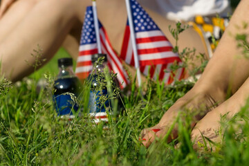 Woman legs and USA flags with soda bottles on grass lawn, celebration of patriotic american...