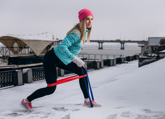 Beautiful sporty woman doing exercises with resistance band outtdoor in the winter.