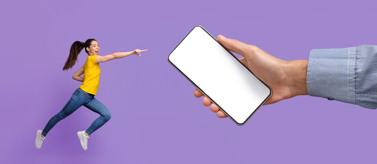 Cheerful lady jumping and pointing at empty smart phone screen