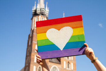 Rainbow heart placard sign, symbol of LGBT love. Pride Parade equality march in Krakow, Poland to support and celebrate LGBT+, LGBTQ. Saint Mary's Basilica (Mariacki Church Kraków) in background. - obrazy, fototapety, plakaty