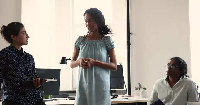 Smiling young African woman project coordinator interact with diverse teammates of Indian ethnicity offer effective problem solution. Skilled millennial lady manager consult colleagues at workplace