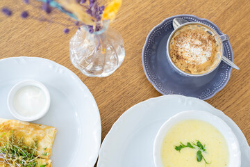 Morning breakfast with cheese soup, coffee, croutons, pancakes and greens against the background of backlight.