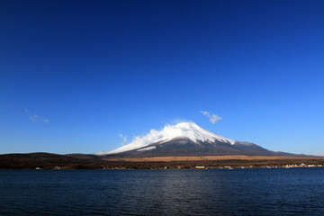 Fuji mountain with snow and fog covered top, lake or sea and clear blue sky background with copy space. This place famous in Japan and Asia for people travel to visit and take picture.