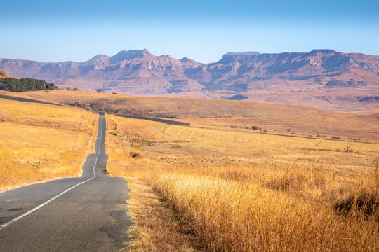 A tarmac road cuts through the dry, arid landscape of Kwazulu Natal near Drakensberg, South Africa.