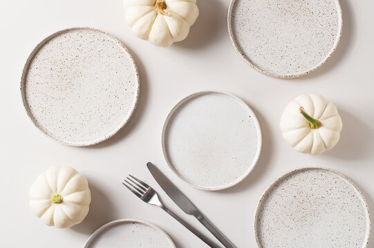 Some white ceramic plates with tableware and pumpkins serving background