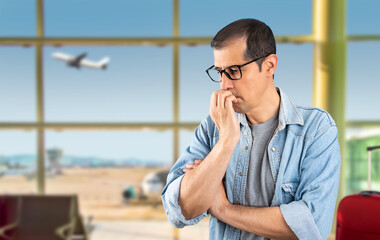 Adult hispanic man with glasses at the airport looking stressed and nervous with hand on mouth biting his nails and anxiety problem because of fear of the plane