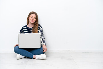 Young caucasian woman with a laptop sitting on the floor isolated on white background posing with arms at hip and smiling