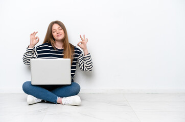 Young caucasian woman with a laptop sitting on the floor isolated on white background in zen pose