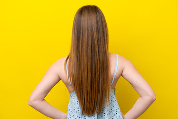 Young caucasian woman isolated on yellow background in back position