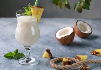 Summer. Drinks and cocktails. Pina colada in glass with pineapple, coconut, mint and a branch of greenery on a light gray background. Background image, copy space - obrazy, fototapety, plakaty