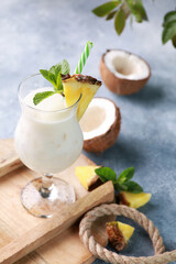 Summer. Drinks and cocktails. Pina colada in glass with pineapple, coconut, mint and a branch of greenery on a light gray background. Background image, copy space