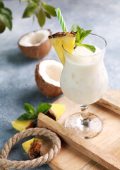 Summer. Drinks and cocktails. Pina colada in glass with pineapple, coconut, mint and a branch of greenery on a light gray background. Background image, copy space