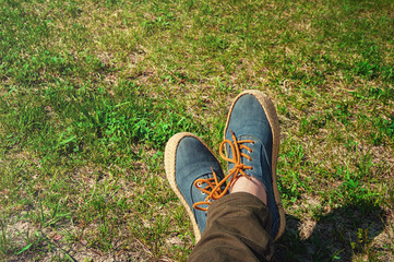 Female feet in jeans sneakers on the background of grass.	