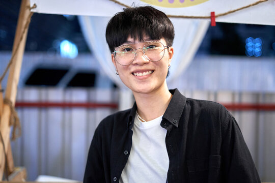 Portrait of a non binary person in casual clothes and glasses in a night market