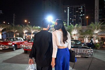 Lesbian couple standing in a parking lot full of vintage cars in a night fair