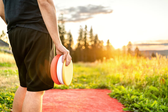 Disc golf in summer at sunset. Man with frisbee equipment in park course. Guy playing discgolf. Player in outdoor sport tournament. Landscape in Finland.