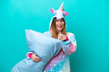 Young caucasian girl with unicorn pajamas holding pillow isolated on blue background surprised and pointing front