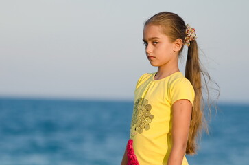Fototapeta na wymiar Girl at sunset. beautiful little girl in a yellow T-shirt against the evening sea