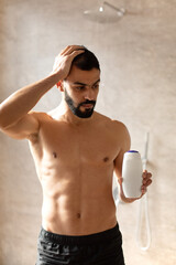 Fototapeta na wymiar Handsome young guy standing with shampoo bottle in hand