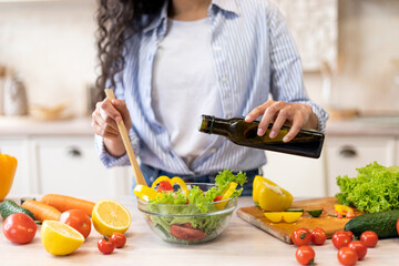 Lady cooking fresh vegetable salad, adding olive oil and seasoning to bowl, enjoying eating healthy...