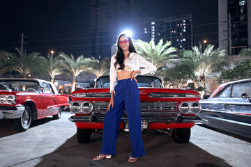 Beauty young woman posing in front of a luxury antique car in a night fair