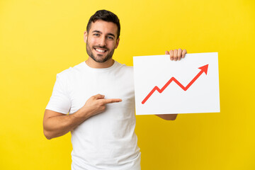 Young handsome caucasian man isolated on yellow background holding a sign with a growing statistics...