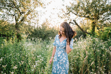Fototapeta na wymiar Portrait of beautiful European woman smiling and looking away at park during sunset. Outdoor portrait of a smiling girl. Happy cheerful girl in blue silk dress 