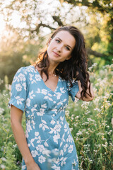Fototapeta premium Portrait of beautiful European woman smiling and looking away at park during sunset. Outdoor portrait of a smiling girl. Happy cheerful girl in blue silk dress 