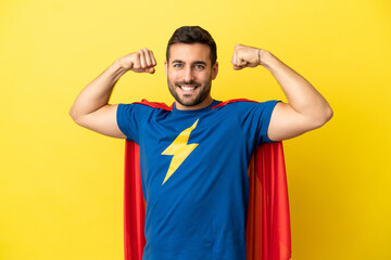 Young handsome caucasian man isolated on yellow background in superhero costume and doing strong...