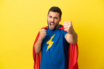 Young handsome caucasian man isolated on yellow background in superhero costume and fighting