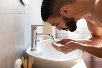 Portrait of bearded man washing his face at bathroom