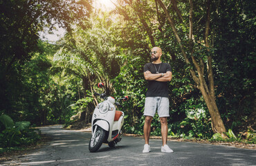 Stylish young man and his motorbike on the road in the jungle