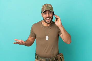 Military with dog tag over isolated on blue background keeping a conversation with the mobile phone...
