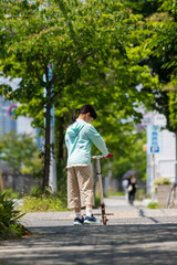 Fototapeta na wymiar 夏の住宅地の道路でスクーターを遊んでいる小学生の女の子の姿
