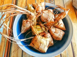 fully cooked ketupat in a steel pot on a wooden table. malaysian traditional food often eat during eid al-fitr or hari raya aidilfitri. ketupat is made from coconut leaves and inside it is packed rice