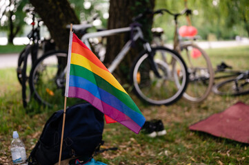 LGBTIQ+ community having picnic in park on spring day. Rainbow flag flying, backpacks and bicycles.