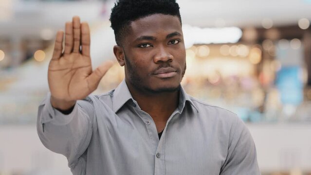 Close-up of young serious confident african american man looking at camera puts forward palm showing stop gesture demonstrating protection personal boundaries protest against violence racism refusal