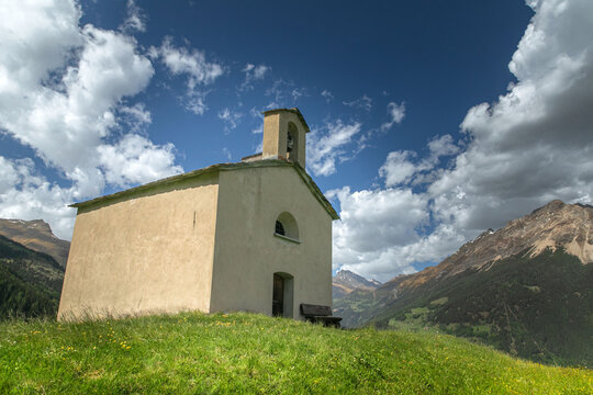 An old church on top of a mountain among the Alps. Switzerland, Canton of Graubunden. Poschiavo. Spring blooming alpine meadows. Switzerland