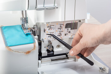 Hand with tweezers puts the thread in the mechanism of the sewing machine