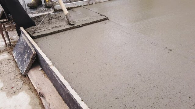 Construction worker uses bullfloat to flatten cement mortar screed. Concrete works on construction site. Cast-in-place work using trowels. 