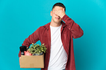Young caucasian man making a move while picking up a box full of things isolated on blue background...
