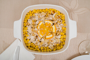 Healthy chicken meat salad with corn and pine nuts in a white salad bowl on the table.