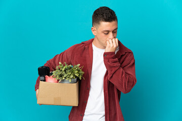 Young caucasian man making a move while picking up a box full of things isolated on blue background...