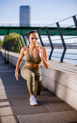 Young woman in sportswear stretching on a river promenade