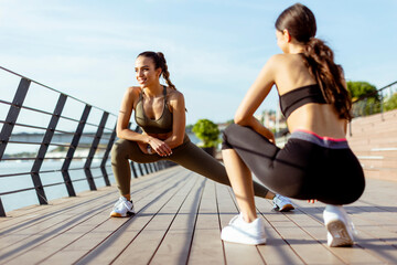 Young women in sportswear exercising on a river promenade
