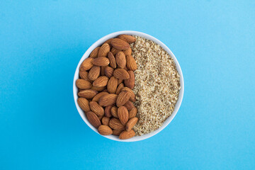 Dried whole and chopped almond in the white bowl on the blue background. Top view. Closeup.
