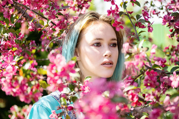 Portrait of blue haired woman against pink blossom trees at sunny day.